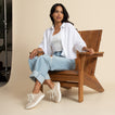 Woman seated on wooden chair wearing Reef Neptune beige sneakers facing left, showcasing comfort and surf-inspired style.