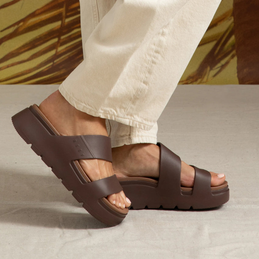 Cali Solana brown platform sandals on feet, right foot lifted showing sole, water-friendly durable slip-on beach footwear