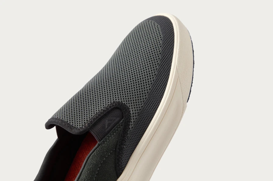 Close-up view of the grey slip-on sneaker facing slightly left, showing breathable mesh upper and cushioned sole edge.
