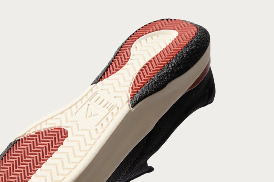 Close-up of the slip-on sneaker sole facing upward, showing textured red and white outsole with black cushioning edge.